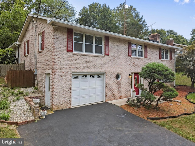 view of front of house featuring aphalt driveway, brick siding, a chimney, fence, and a garage