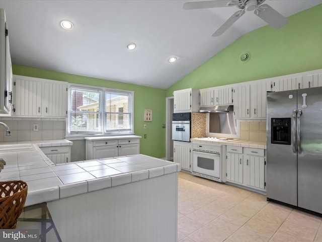 kitchen featuring light tile patterned floors, tile counters, appliances with stainless steel finishes, a sink, and under cabinet range hood