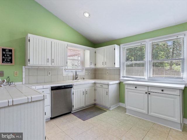 kitchen with tile counters, dishwasher, lofted ceiling, white cabinetry, and a sink