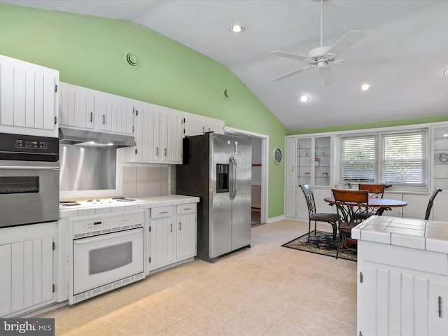 kitchen featuring tile countertops, under cabinet range hood, stainless steel appliances, and lofted ceiling