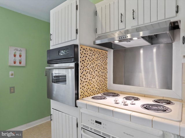 kitchen with light tile patterned floors, tasteful backsplash, tile counters, oven, and under cabinet range hood