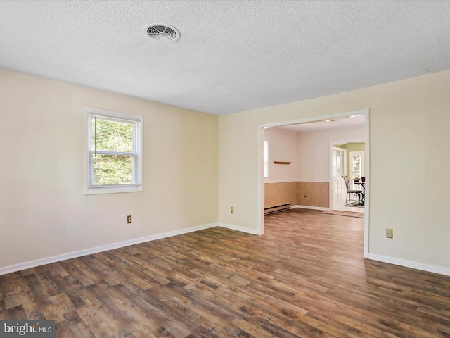 empty room featuring baseboards, visible vents, dark wood finished floors, a baseboard radiator, and a textured ceiling