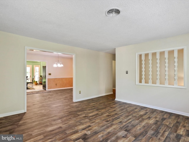 empty room with dark wood finished floors, visible vents, an inviting chandelier, a textured ceiling, and baseboards