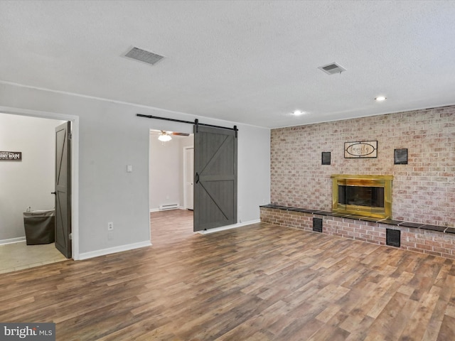 unfurnished living room with a brick fireplace, a barn door, visible vents, and wood finished floors