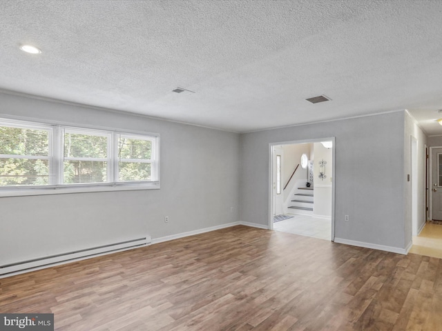 empty room with baseboards, visible vents, stairway, wood finished floors, and baseboard heating