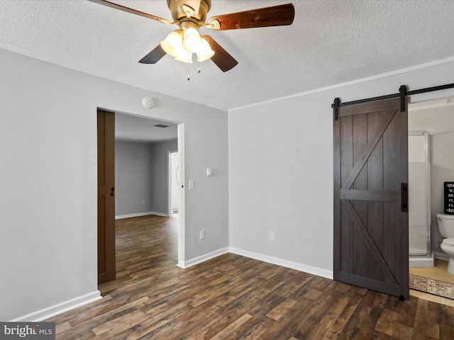 spare room featuring a barn door, ceiling fan, a textured ceiling, wood finished floors, and baseboards