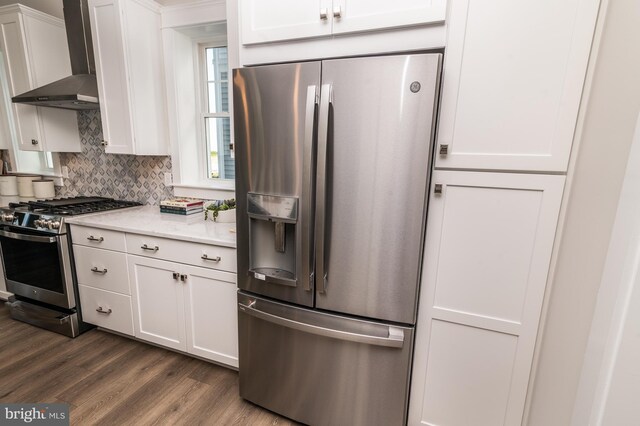 kitchen with appliances with stainless steel finishes, backsplash, white cabinetry, wall chimney exhaust hood, and wood-type flooring