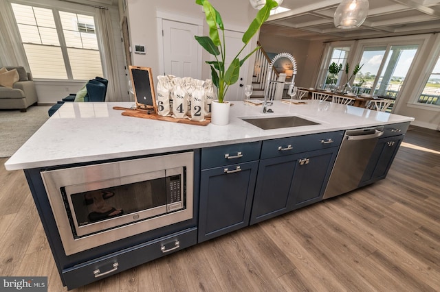 kitchen with appliances with stainless steel finishes, a kitchen island with sink, a sink, wood finished floors, and coffered ceiling