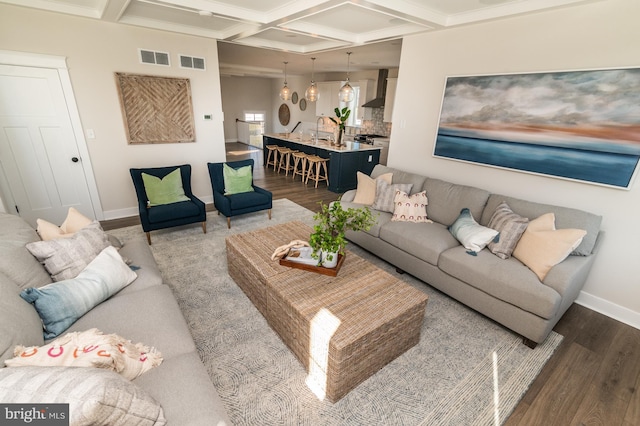 living room featuring dark wood-style flooring, coffered ceiling, visible vents, and baseboards