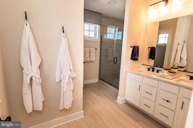 bathroom with a stall shower, a sink, baseboards, and double vanity