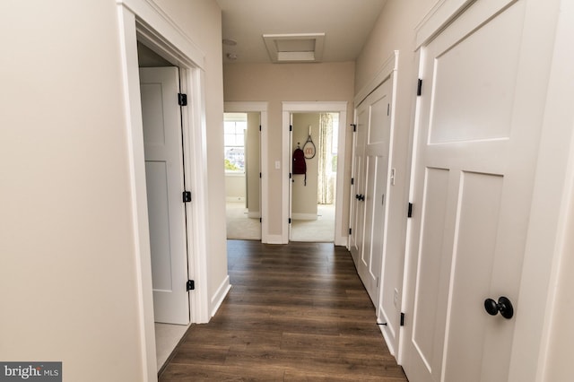 hall featuring dark wood-type flooring, attic access, and baseboards