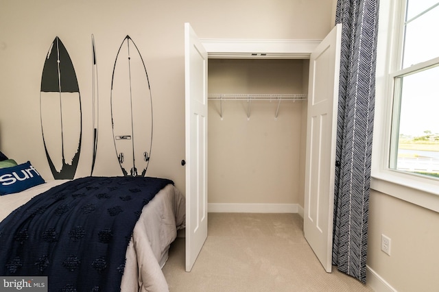 bedroom with multiple windows, baseboards, a closet, and light colored carpet