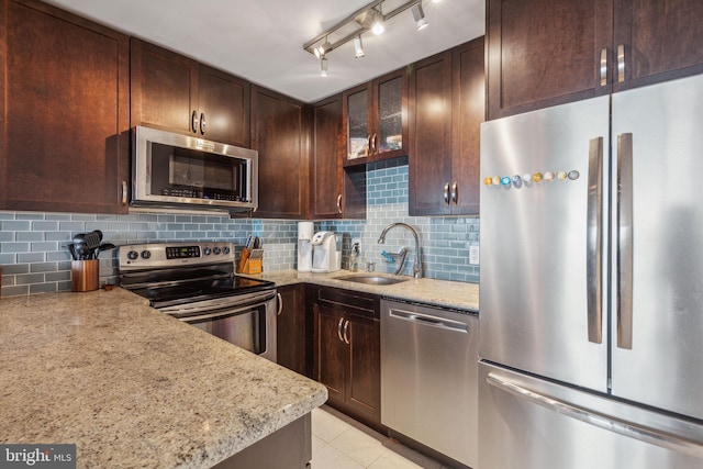 kitchen with backsplash, appliances with stainless steel finishes, a sink, dark brown cabinetry, and light stone countertops