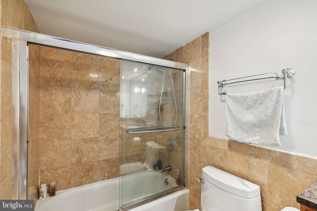 full bathroom with bath / shower combo with glass door, toilet, and tile walls