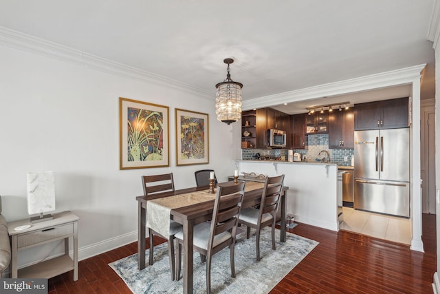 dining room with dark wood-type flooring, ornamental molding, and an inviting chandelier