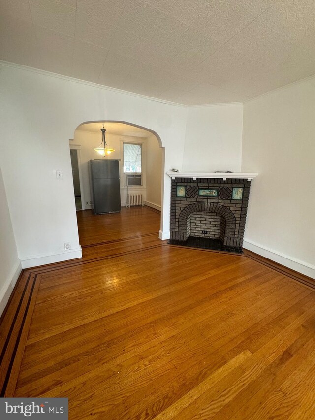 unfurnished living room with hardwood / wood-style flooring, crown molding, a brick fireplace, and radiator