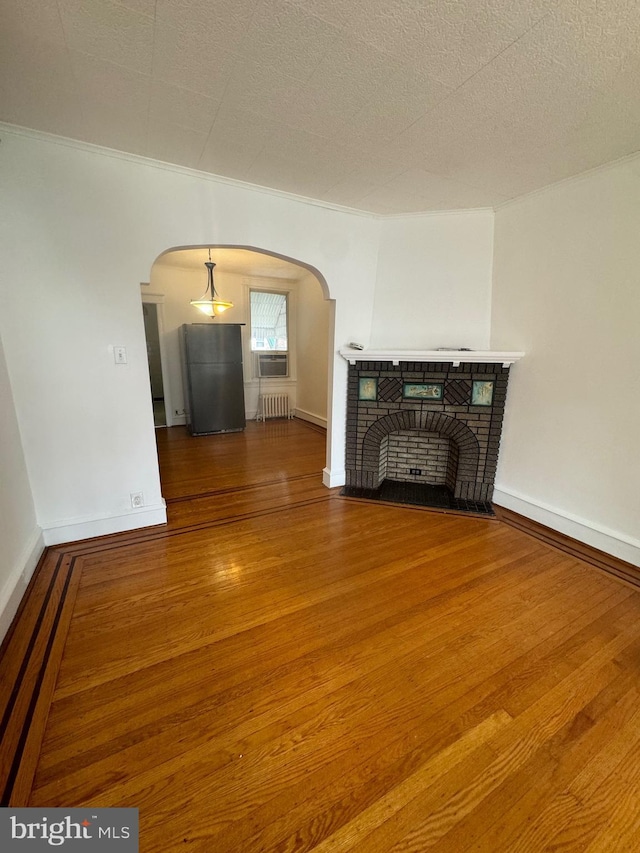 unfurnished living room featuring arched walkways, radiator, a fireplace with flush hearth, wood finished floors, and baseboards