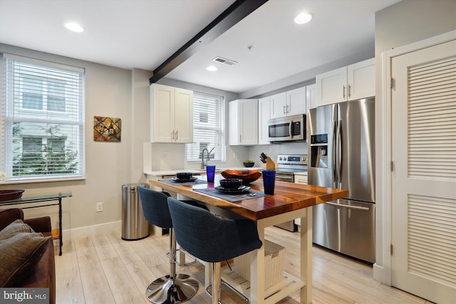 kitchen with light hardwood / wood-style flooring, stainless steel appliances, white cabinets, and beam ceiling