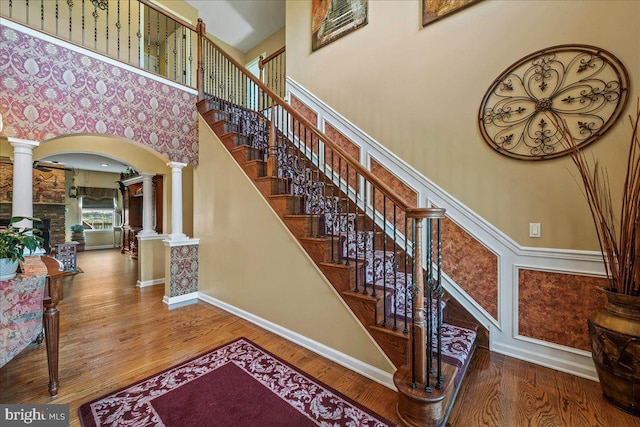 stairway with a towering ceiling, hardwood / wood-style floors, and ornate columns