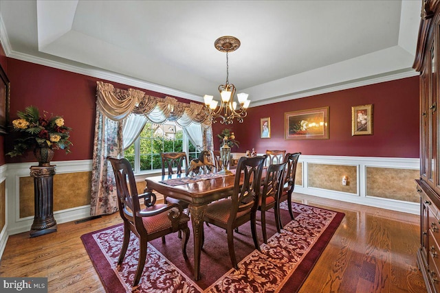 dining room with light wood-type flooring, crown molding, an inviting chandelier, and a tray ceiling