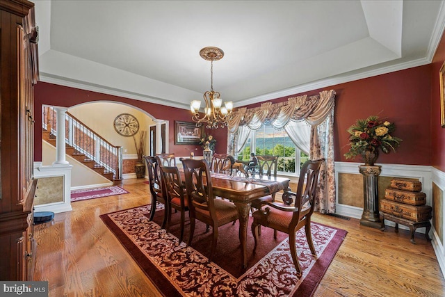 dining area featuring a tray ceiling, light hardwood / wood-style floors, a chandelier, and ornate columns