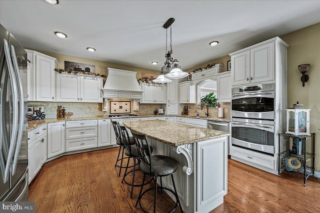 kitchen featuring decorative backsplash, custom range hood, hardwood / wood-style floors, white cabinets, and stainless steel appliances