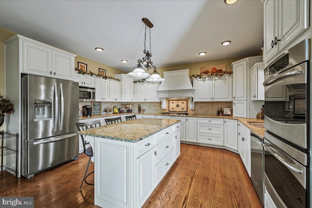 kitchen featuring hardwood / wood-style floors, backsplash, appliances with stainless steel finishes, a kitchen island, and premium range hood