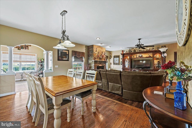 dining room with ceiling fan, decorative columns, wood-type flooring, and a fireplace