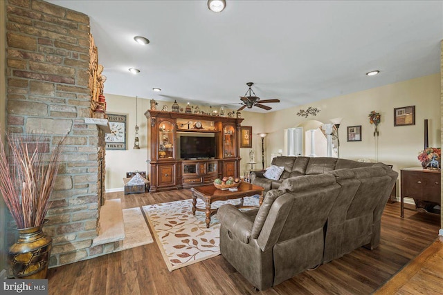 living room with ceiling fan, dark hardwood / wood-style floors, brick wall, and a fireplace