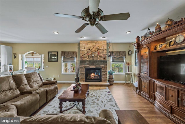 living room featuring ceiling fan, light hardwood / wood-style flooring, a stone fireplace, and plenty of natural light