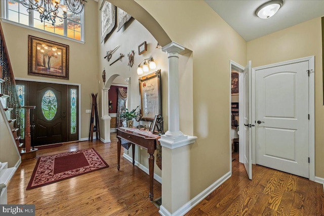 foyer featuring a high ceiling, ornate columns, a chandelier, and wood-type flooring