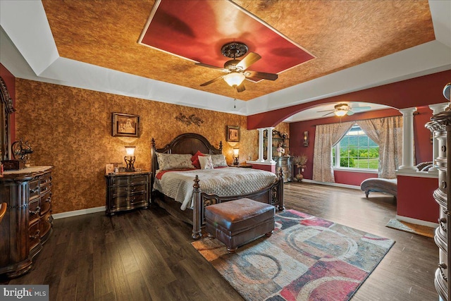 bedroom with dark hardwood / wood-style flooring, ceiling fan, a tray ceiling, and ornate columns