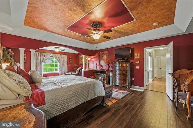 bedroom with a tray ceiling, ceiling fan, decorative columns, and wood-type flooring