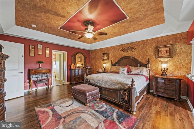 bedroom with ceiling fan, ensuite bath, a tray ceiling, and hardwood / wood-style floors