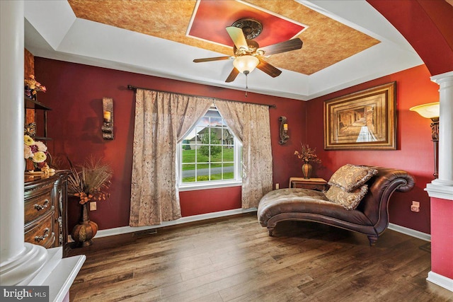 sitting room featuring ceiling fan, a tray ceiling, dark wood-type flooring, and ornate columns