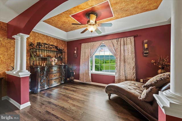 living area with a tray ceiling, ceiling fan, decorative columns, and dark hardwood / wood-style floors