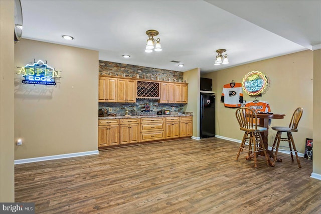 kitchen featuring decorative backsplash, black refrigerator, hardwood / wood-style floors, and stone counters