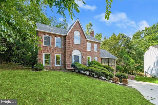 colonial-style house featuring a sunroom, a front yard, a chimney, and brick siding