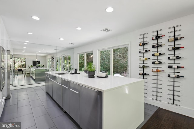 kitchen with sink, dark tile patterned floors, plenty of natural light, and an island with sink