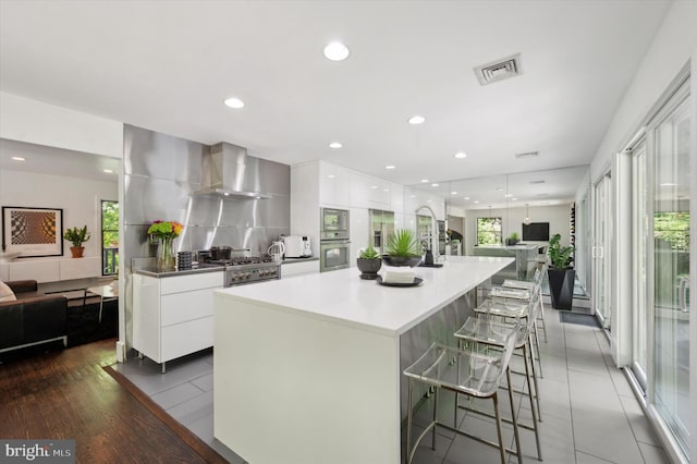 kitchen featuring a spacious island, appliances with stainless steel finishes, hardwood / wood-style flooring, wall chimney exhaust hood, and white cabinets