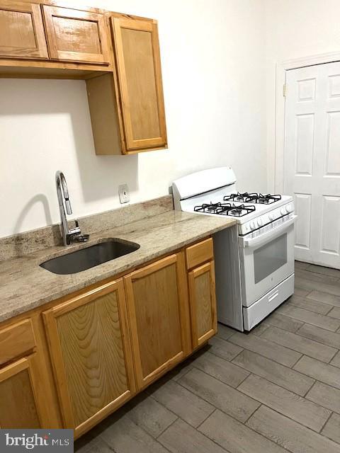 kitchen with sink, light stone counters, dark hardwood / wood-style floors, and white gas stove