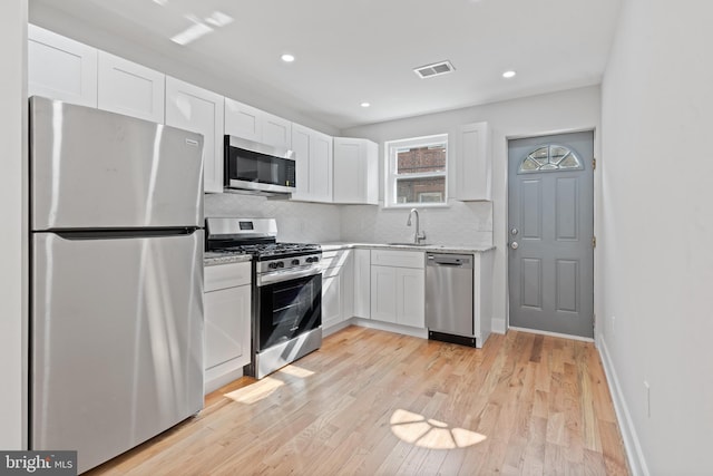 kitchen with light hardwood / wood-style flooring, stainless steel appliances, decorative backsplash, and white cabinetry