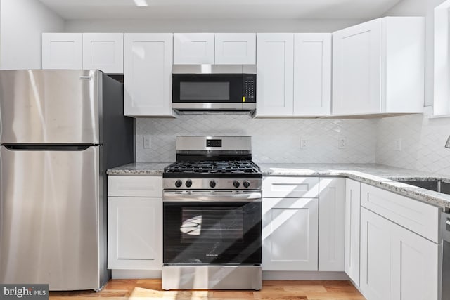 kitchen featuring backsplash, light stone counters, stainless steel appliances, light hardwood / wood-style floors, and white cabinetry