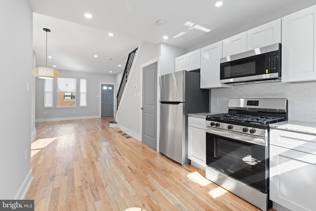 kitchen with light hardwood / wood-style flooring, light stone countertops, stainless steel appliances, white cabinetry, and tasteful backsplash