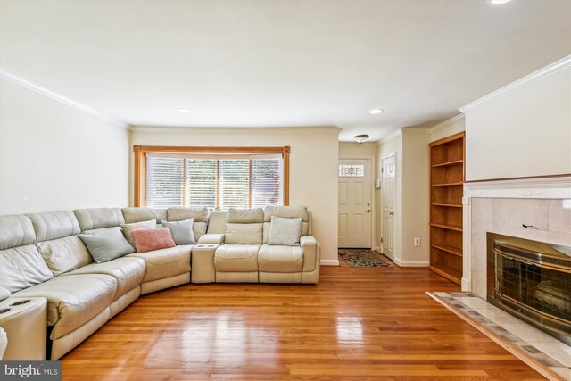 unfurnished living room with built in shelves, crown molding, light hardwood / wood-style floors, and a tiled fireplace