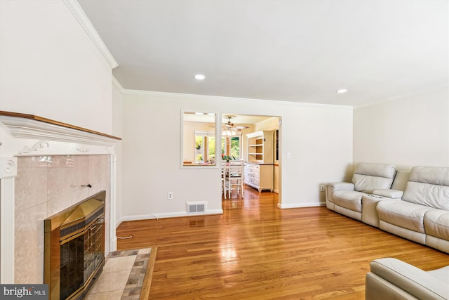 living room with ceiling fan, light hardwood / wood-style floors, crown molding, and a tile fireplace