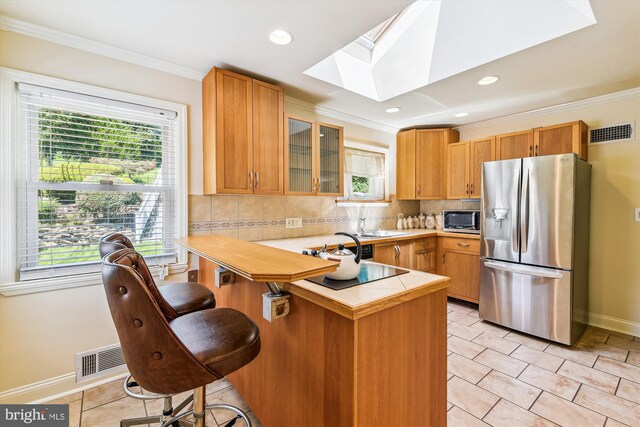 kitchen featuring appliances with stainless steel finishes, backsplash, a skylight, light tile patterned floors, and kitchen peninsula