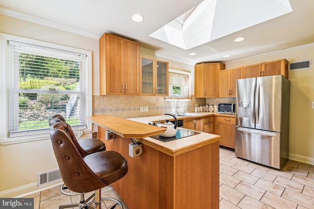 kitchen featuring visible vents, glass insert cabinets, appliances with stainless steel finishes, a peninsula, and a kitchen bar