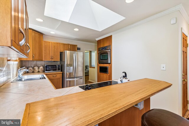 kitchen with sink, appliances with stainless steel finishes, a skylight, decorative backsplash, and kitchen peninsula