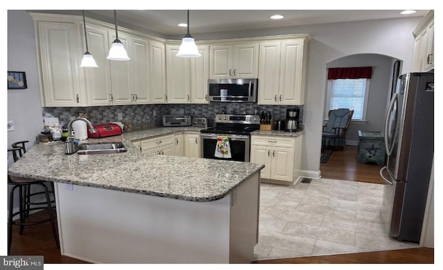 kitchen with kitchen peninsula, a kitchen breakfast bar, sink, pendant lighting, and stainless steel appliances